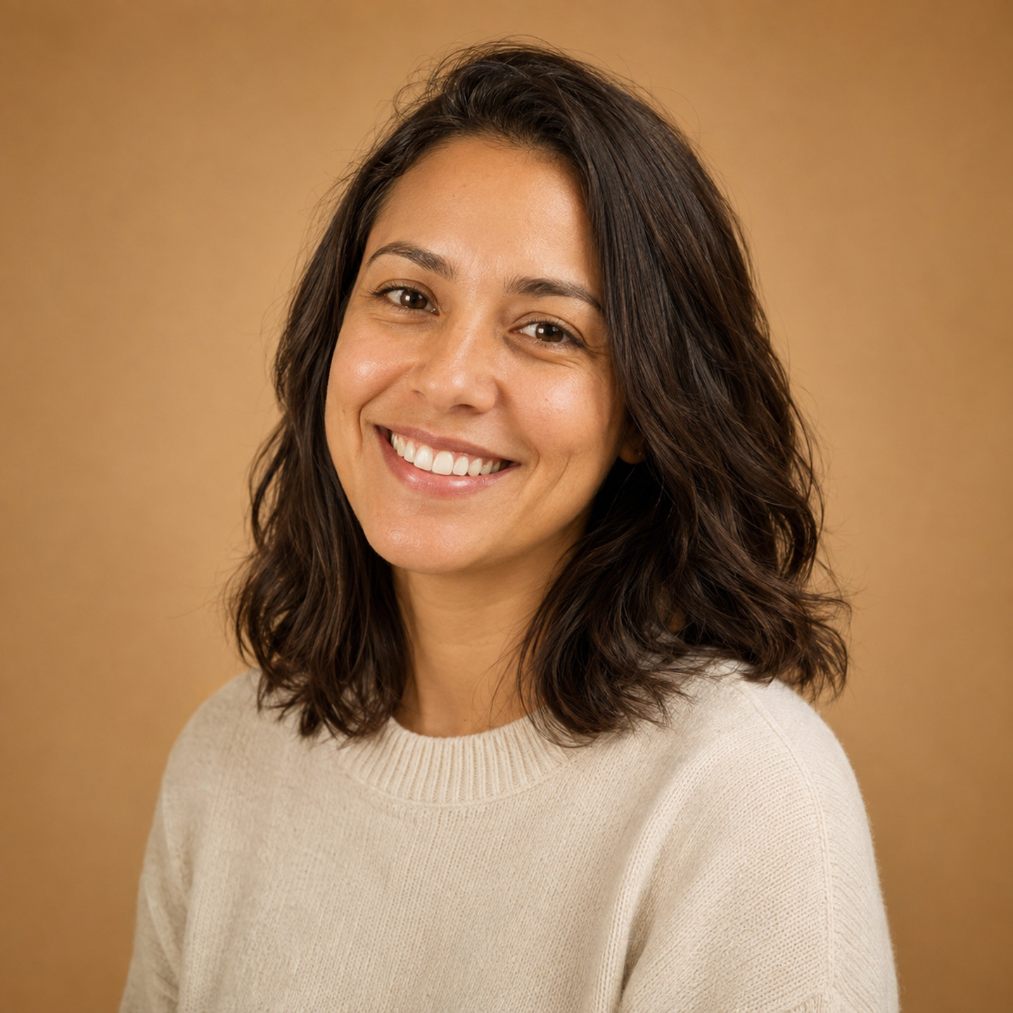 A woman in a cream knit sweater against a warm tan studio backdrop